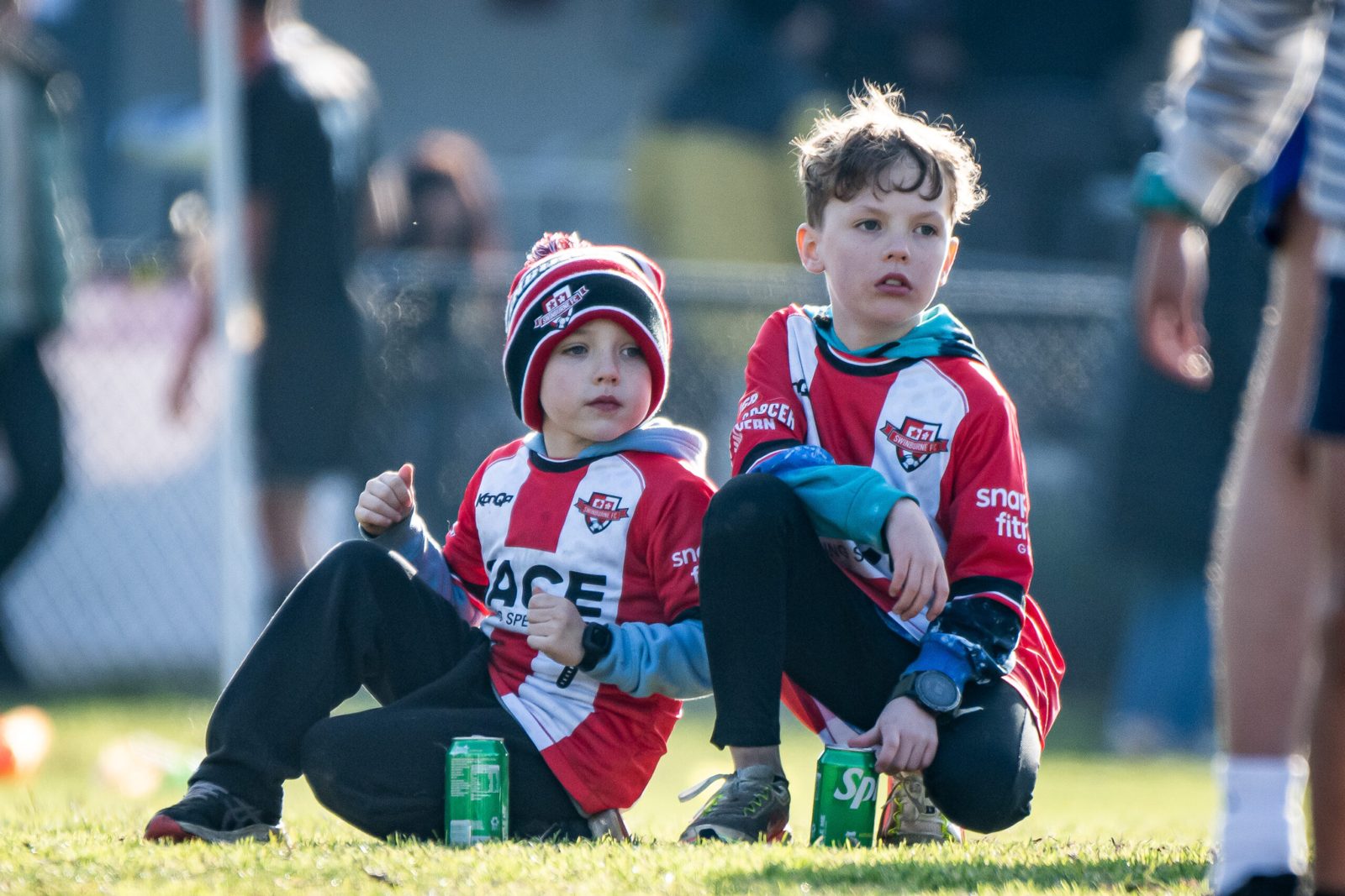 Two young fans in Swinburne FC kits watching from the sideline
